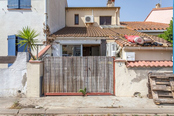 A residential building with a tiled roof, a wooden fence, and a small plant in front.