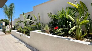 Ein moderner Außenbereich mit einem Betonpflanzgefäß, bepflanzt mit verschiedenen Pflanzen und einer kleinen roten Blume.