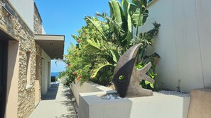A narrow pathway flanked by a stone wall and a planter with tropical plants and a decorative sculpture. - Villa Onlysea, 5 Bord de mer (roquebrune sur argens)
