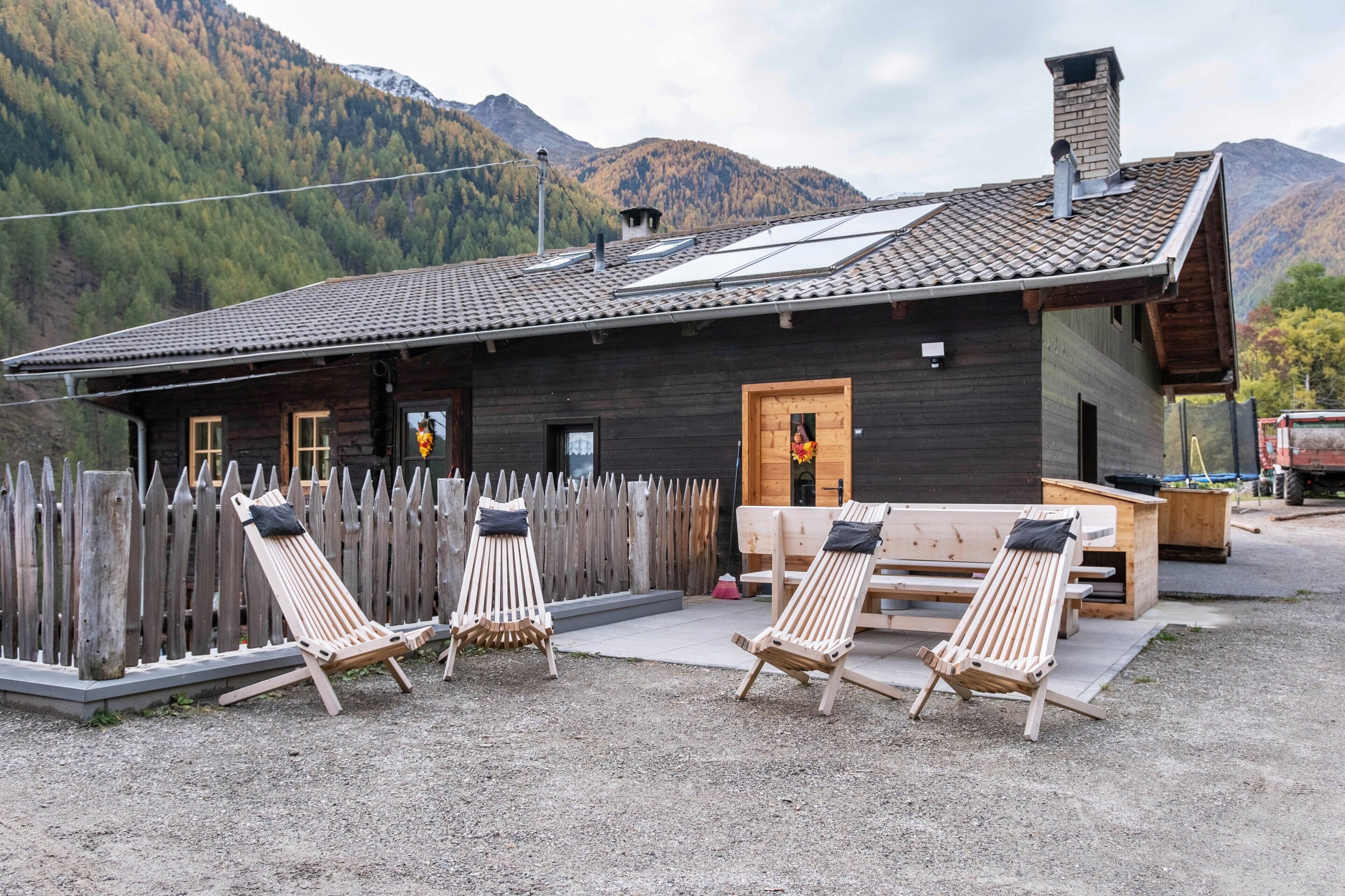 A wooden cabin with a sloped roof, a wooden deck, and a fenced outdoor area with lounge chairs.