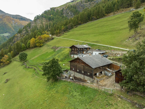 Un chalet traditionnel en bois, doté de fondations en pierre, d’un escalier en pierre et d’une cour clôturée avec un petit enclos pour animaux.
