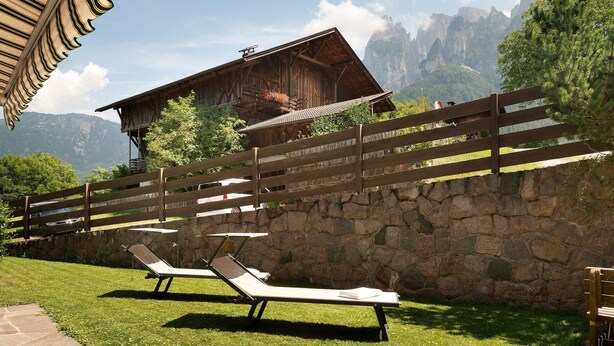 Una cabaña de madera con pared de piedra, dos tumbonas y una valla de madera.