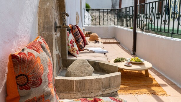 A balcony with a stone bench, a small table with a plate of fruit, and a patterned cushion. - Holiday Home '1900's Traditional House in Asklipio' with Private Terrace, Wi-Fi and Air Conditioning (Rhodes)