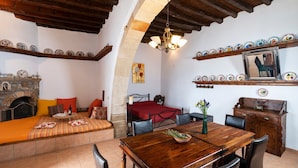 A room with a wooden dining table, chairs, a fireplace, a bed with a red bedspread, and decorative plates on the walls. - Holiday Home '1900's Traditional House in Asklipio' with Private Terrace, Wi-Fi and Air Conditioning (Rhodes)