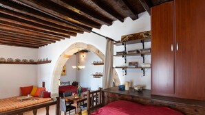 A room with a wooden ceiling, a red bed, a wooden table with chairs, and a bookshelf. - Holiday Home '1900's Traditional House in Asklipio' with Private Terrace, Wi-Fi and Air Conditioning (Rhodes)