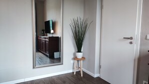 Un pasillo con un espejo grande, una planta en maceta sobre un taburete, un armario de madera y una puerta blanca.