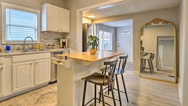 A modern kitchen with white cabinets, a wooden countertop, and a bar area with stools. - 5 Mins From Fountain Square ! (Indianapolis)