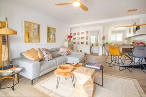 A modern living room with a grey sofa, wooden side tables, and a dining area with chairs. - Vista Azul Alzira - Luxury Apartment with Sea View (Teulada)