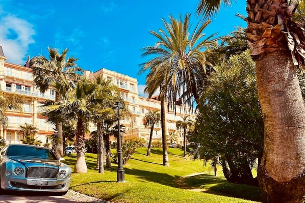 A hotel with a lush garden, palm trees, and a parked car.