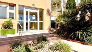 A modern building with a glass entrance, outdoor plants, and a well-maintained garden.