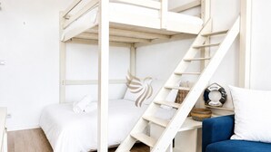 A bunk bed with a wooden ladder, a white bed with rolled towels, a blue sofa, and a welcome sign.