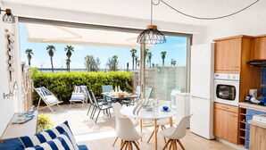 A modern kitchen with a built-in oven and microwave, a dining area with a round table and chairs, and a large sliding glass door leading to a patio with chairs and a view of palm trees.