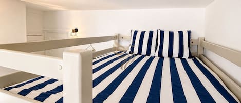 A bunk bed with a striped bedspread, a bedside table, and a wall-mounted light fixture.