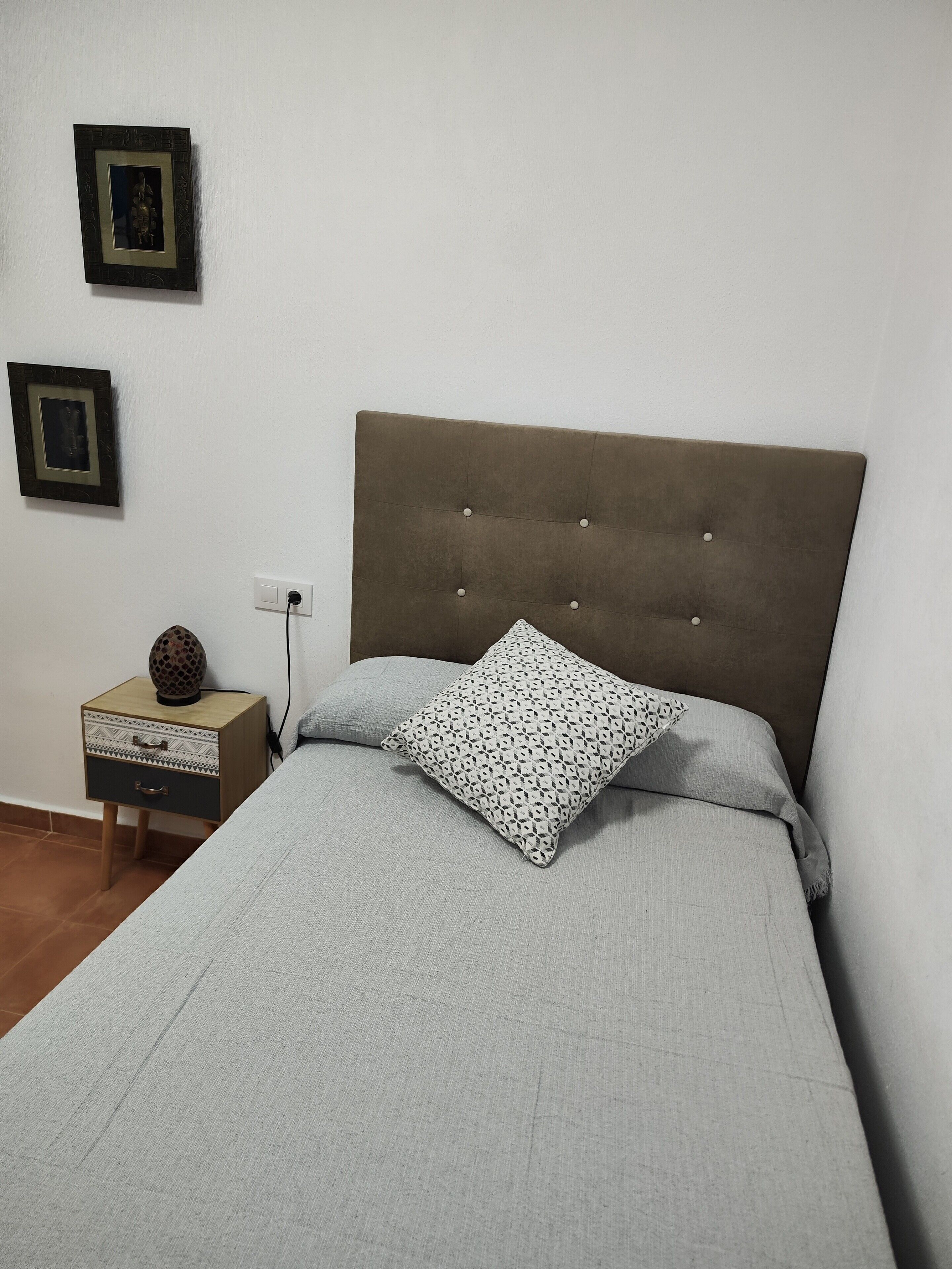 Un dormitorio con cama, una mesita de noche, una lámpara y dos cuadros en la pared.