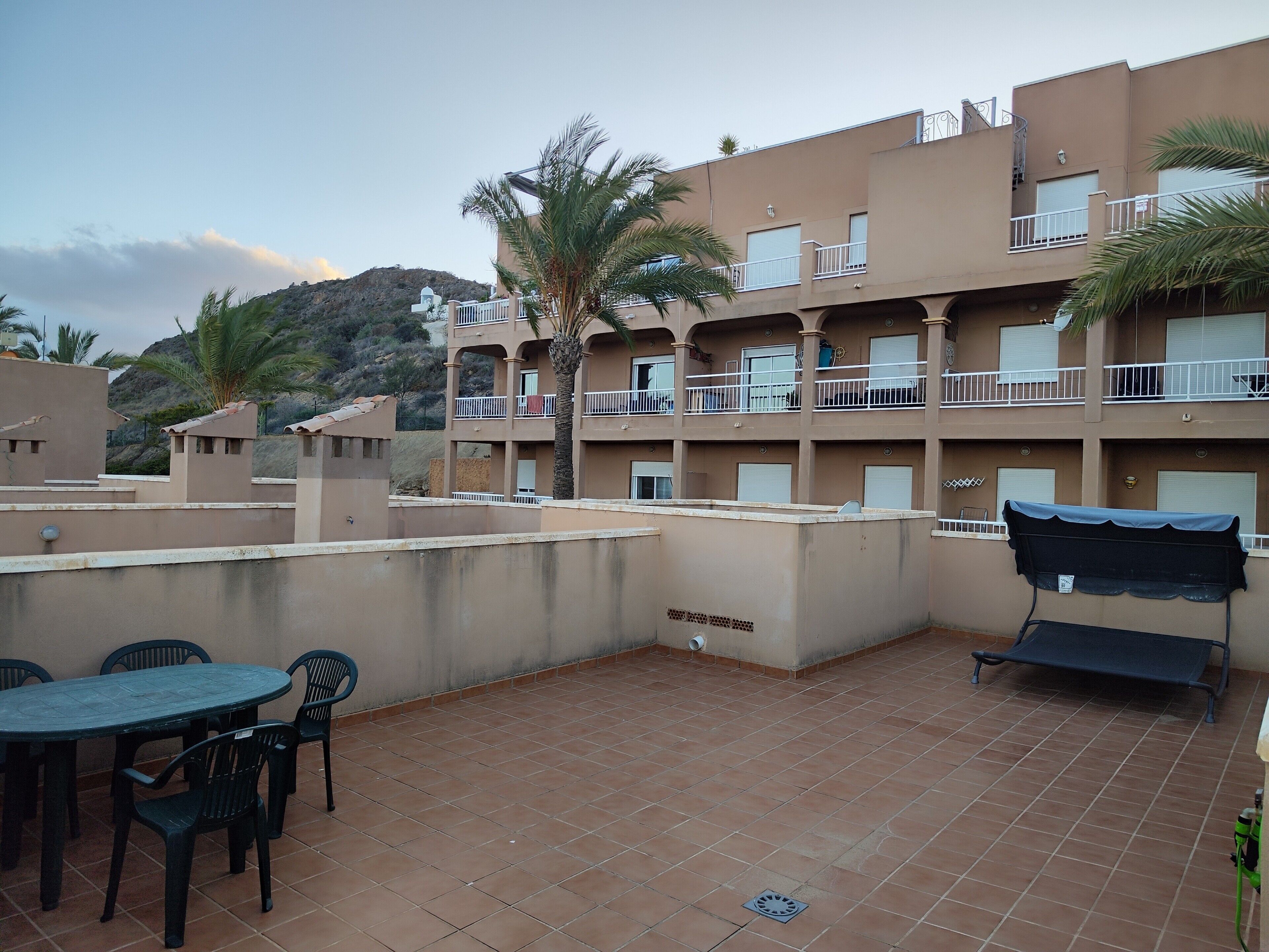 A multi-story building with balconies, a tiled patio area with a table and chairs, and a covered seating area.