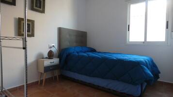 A bedroom with a bed, a nightstand, a wall-mounted shelf, and a window.