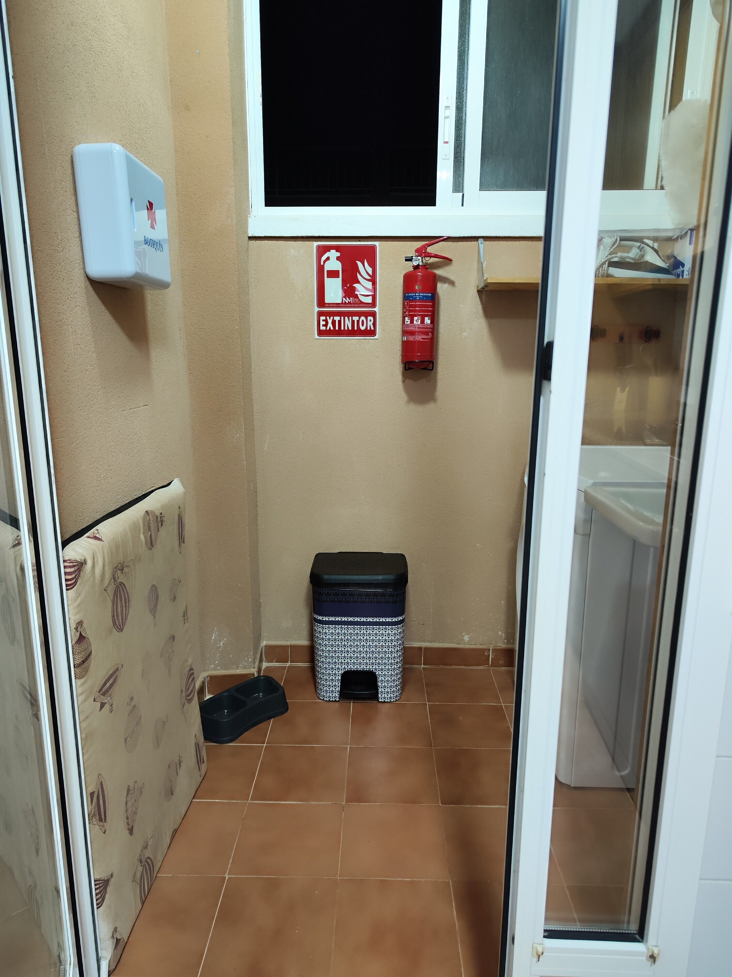 Ein kleines Badezimmer mit Toilette, einem Mülleimer, einem Feuerlöscher und einem Fenster.