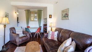Un salon avec un canapé en cuir marron, deux fauteuils, une table à manger avec des chaises et une bibliothèque.