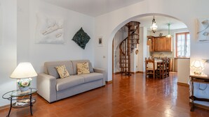 Una sala de estar con un sofá, una mesa con lámpara, una escalera que lleva a una cocina y un comedor.