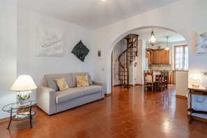 A living room with a sofa, a table with a lamp, a staircase leading to a kitchen, and a dining area.