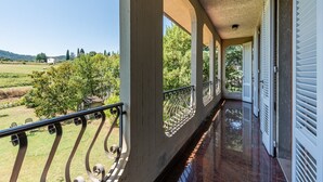 Un balcón con vistas a un paisaje verde, una barandilla y una puerta con contraventanas.
