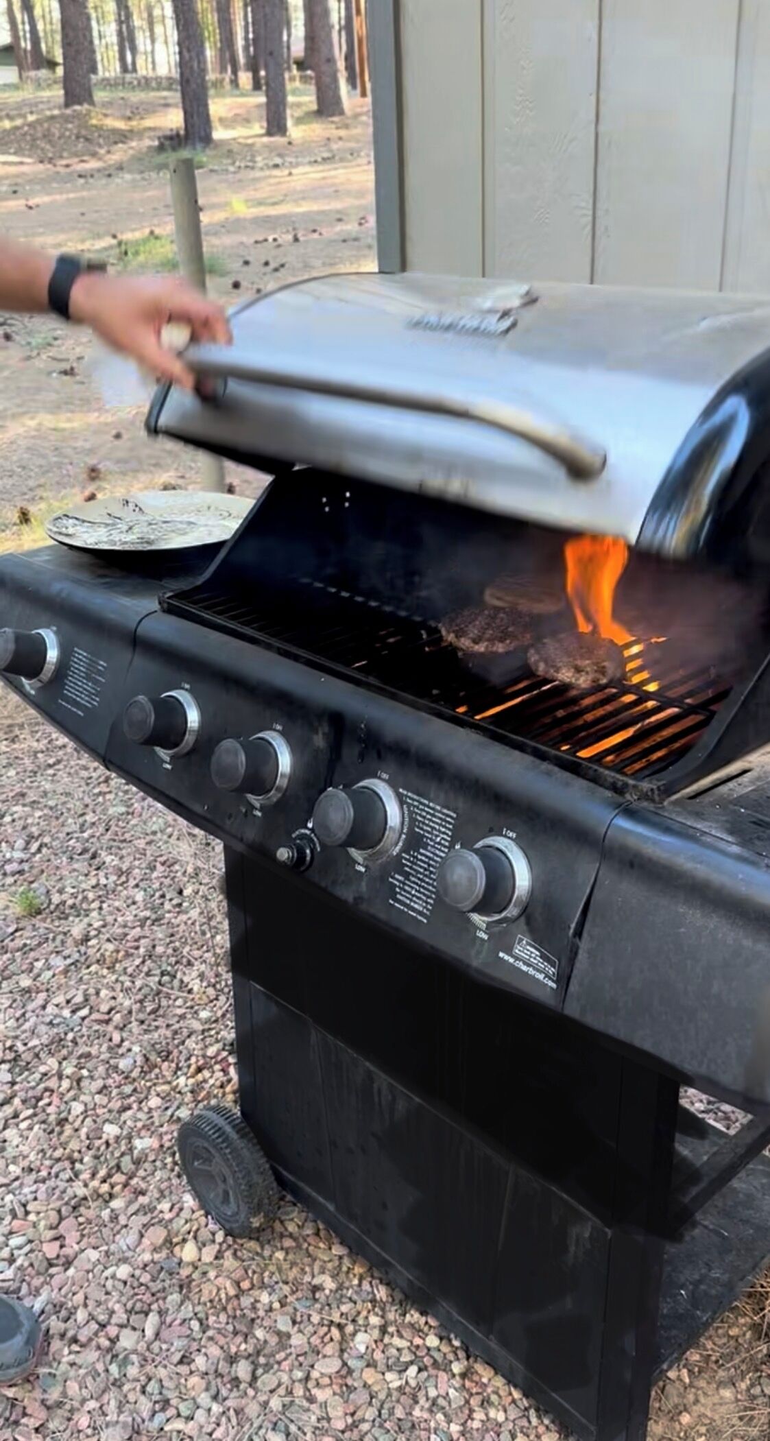 A black barbecue grill with a lid, knobs, and a visible flame.