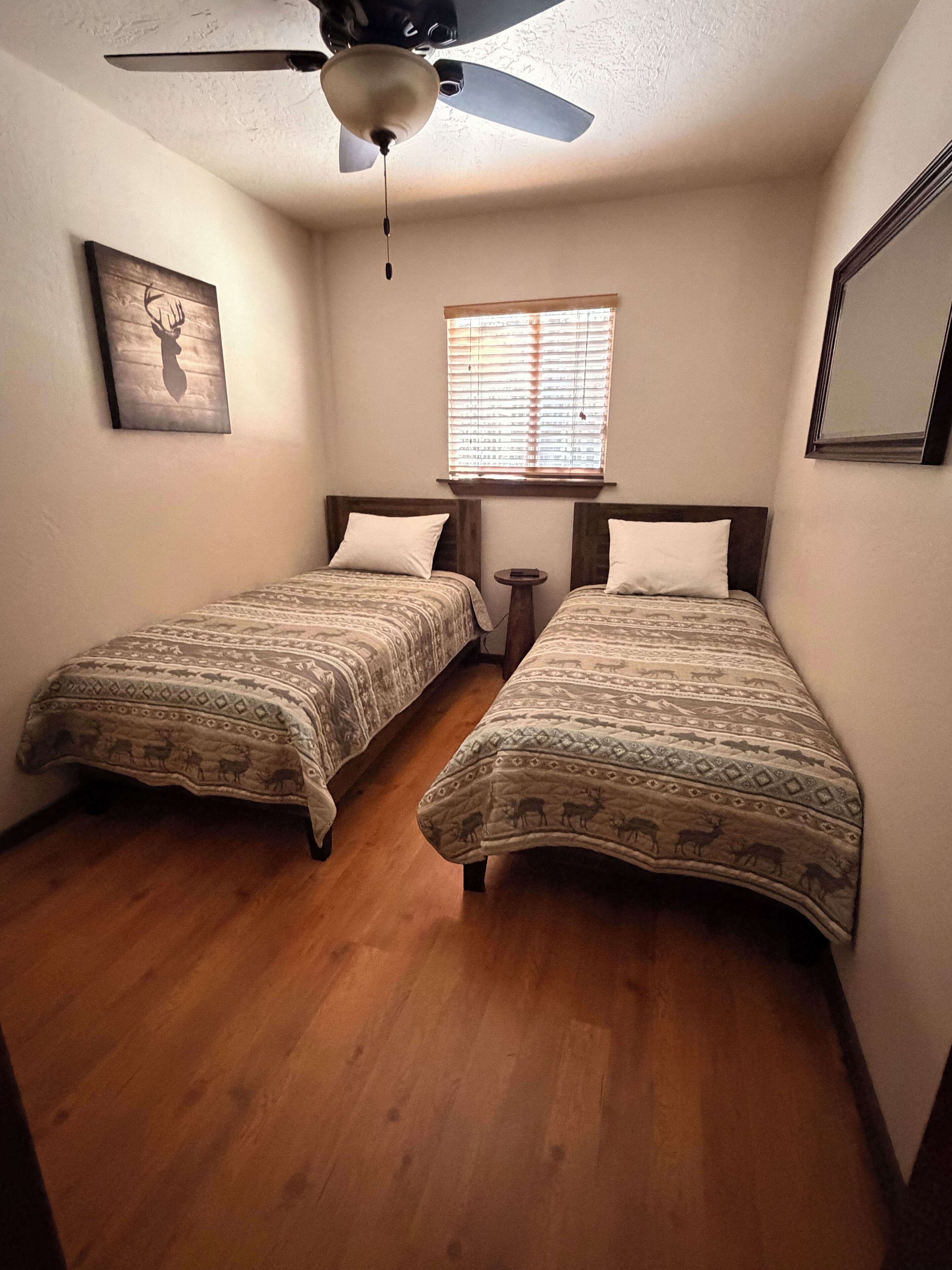 A bedroom with two beds, a ceiling fan, a window with blinds, and a framed picture on the wall.