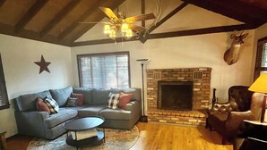 Una sala acogedora con techo de madera, chimenea, sofá y un ciervo montado en la pared.