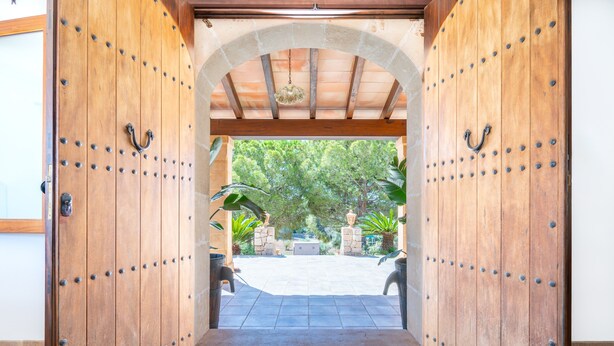 Une porte en bois ouverte donne sur un patio agrémenté d’une arche en pierre, de mobilier d’extérieur et de plantes.
