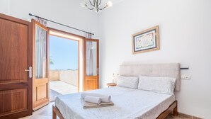 Une chambre à coucher avec un lit, une armoire en bois et une vue sur l’extérieur, visible à travers une porte.