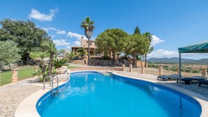 Une piscine bordée de pierres, des chaises longues et une vue sur une maison et des montagnes.