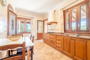 A kitchen with wooden cabinets, a dining table, and a window with curtains. - Villa 'Finca Son Manxo' with Mountain View, Wi-Fi and Air Conditioning (Illes Balears)