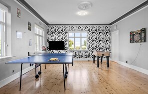 Enjoy games and entertainment in this room with a ping pong table and dartboard, surrounded by windows and a ceiling fan.