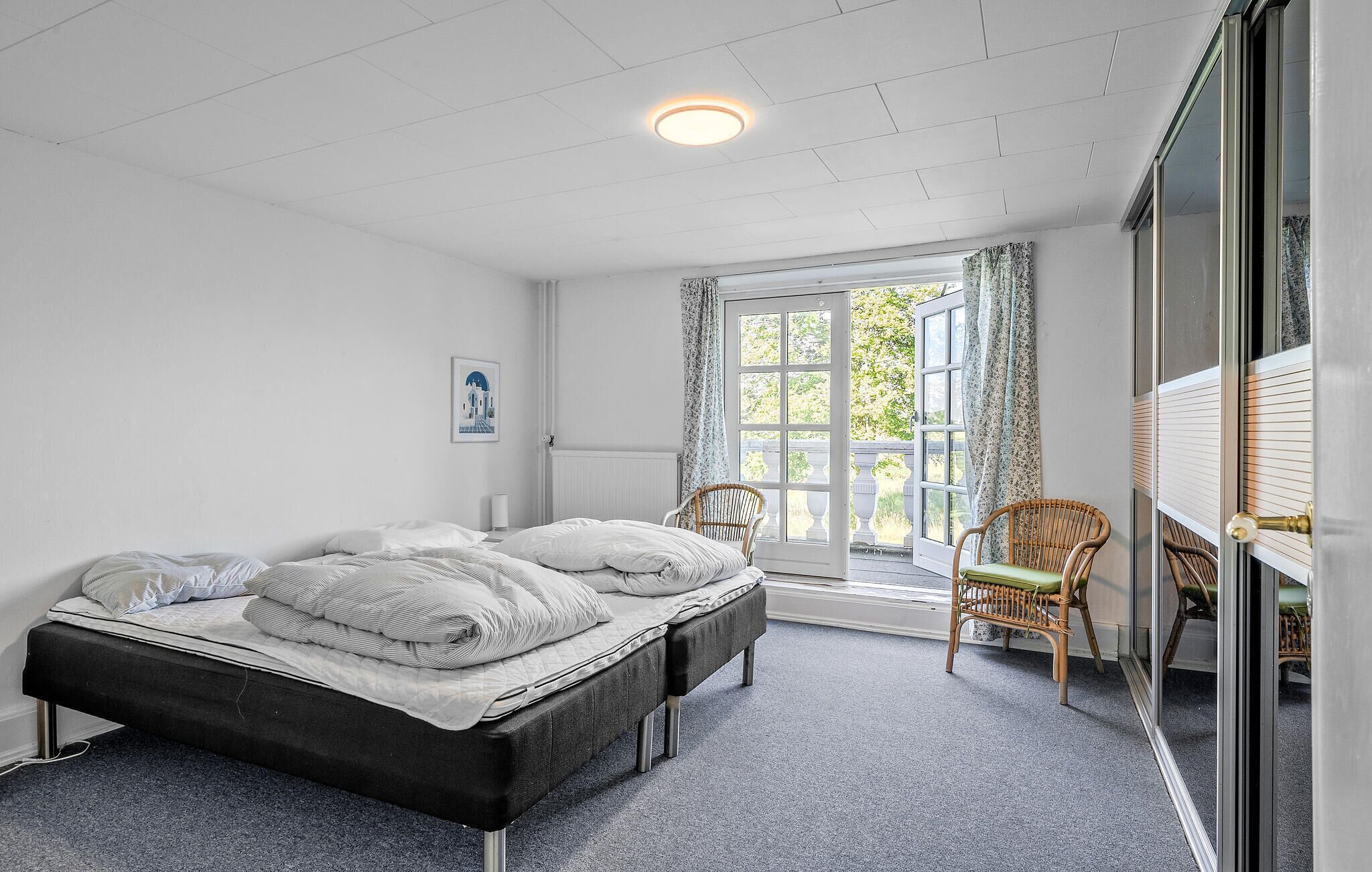 A bedroom with a bed, two chairs, a window with curtains, and a door leading outside.
