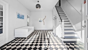 A hallway with a black and white checkered floor, a white staircase, a white bathtub, and a ceiling light fixture. - 5 bedroom nice home in Nyborg (Nyborg)