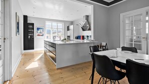 A modern kitchen with a central island, a dining area with a table and chairs, and a view of the outside through large windows. - 5 bedroom nice home in Nyborg (Nyborg)
