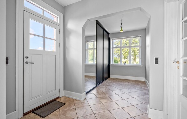 Un couloir avec une porte blanche, une porte noire coulissante et une fenêtre donnant sur des arbres.