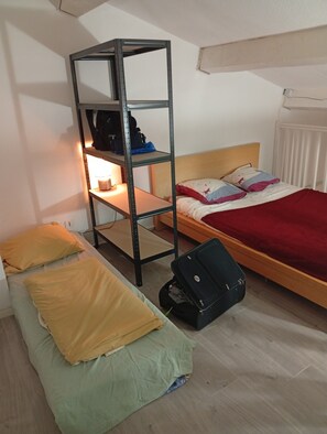 Une chambre de dortoir avec des lits superposés, un bureau avec une lampe, une valise et un radiateur.