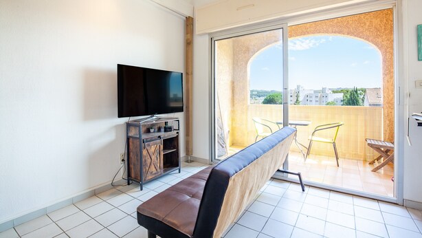 Un balcon avec vue sur les immeubles, un banc, un téléviseur et une porte-fenêtre coulissante.