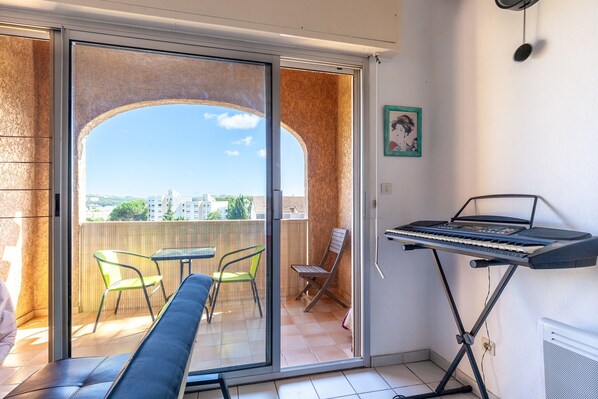 Un balcon avec une porte-fenêtre coulissante, un clavier posé sur un pupitre et une chaise.