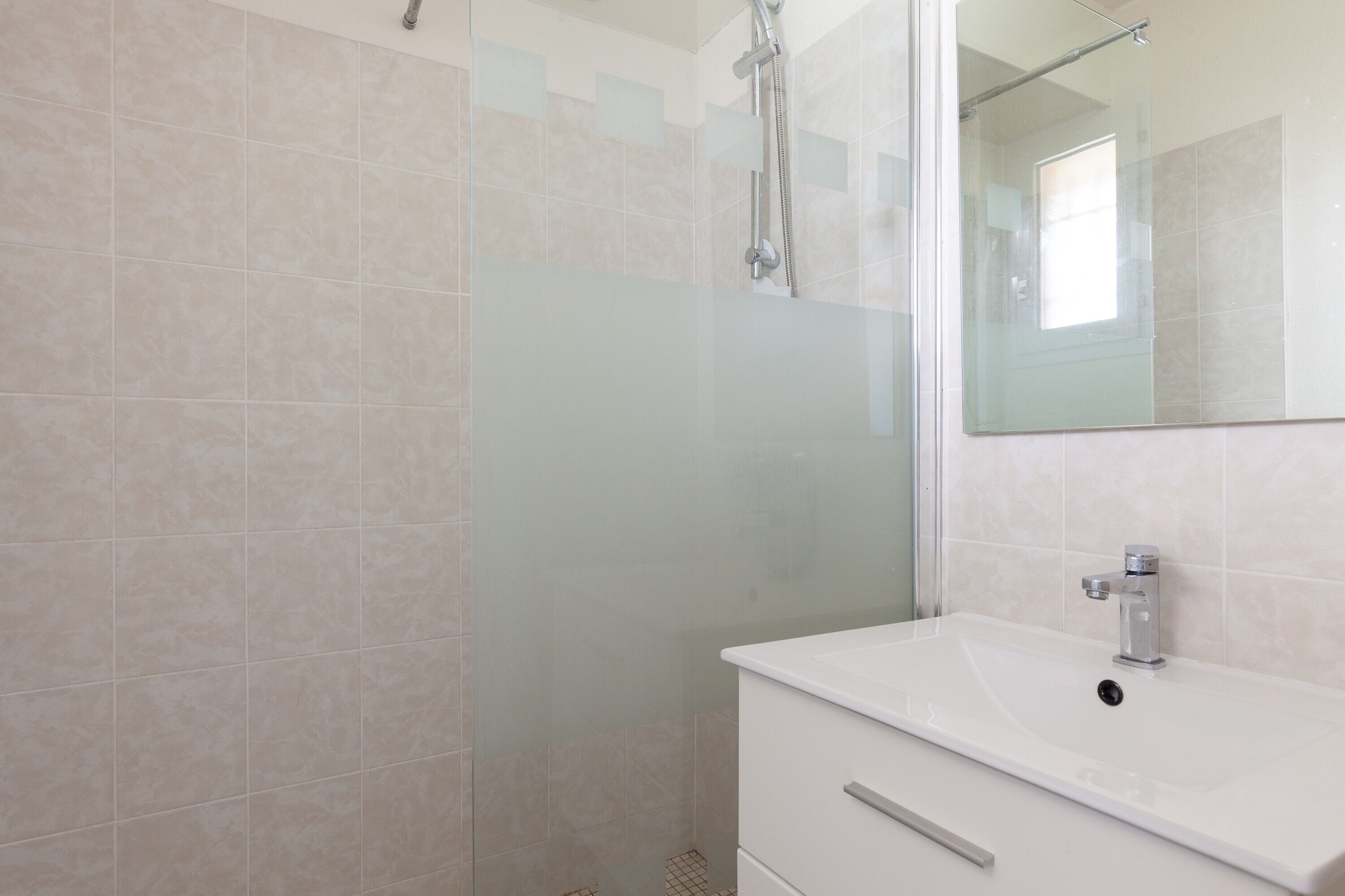 Une salle de bain avec une douche à parois de verre, un lavabo blanc et un miroir.