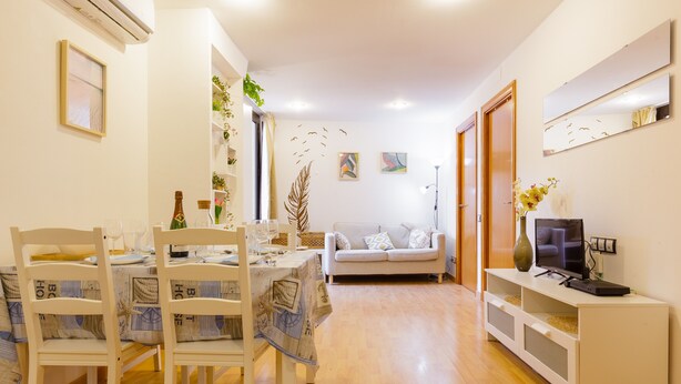 A dining area with a table set for four, a sofa, a TV on a stand, and a bookshelf. - Apartment 'Sauc Beach' with Private Terrace, Wi-Fi and Air Conditioning (Canet de Mar)