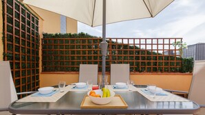 A table set for two with a bowl of fruit, glasses, and a bottle, surrounded by chairs and an umbrella. - Apartment 'Sauc Beach' with Private Terrace, Wi-Fi and Air Conditioning (Canet de Mar)