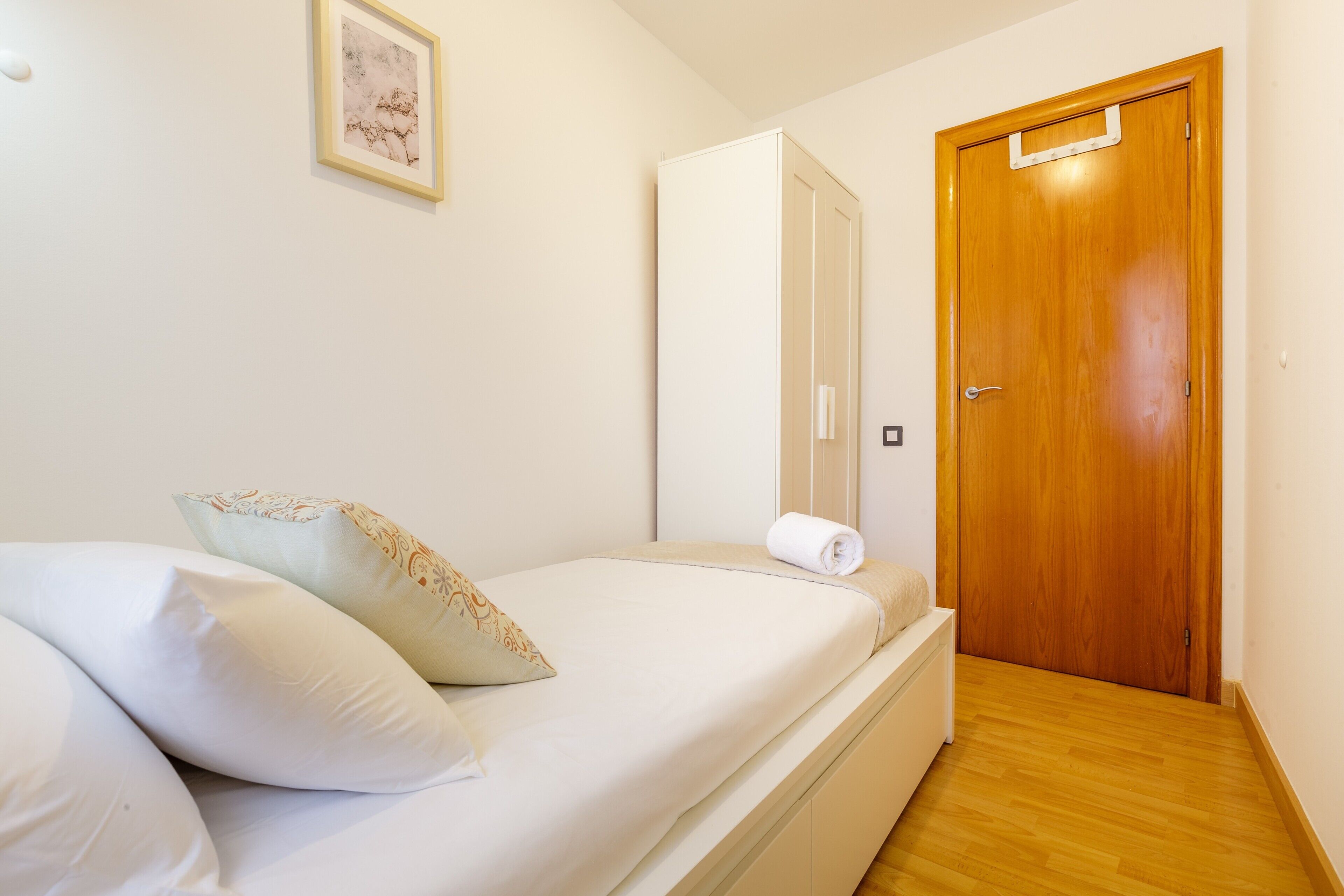 Un dormitorio con una cama, almohadas, una puerta de madera y un cuadro enmarcado en la pared.