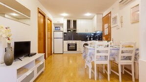 A compact kitchen with a microwave, oven, and sink. There is a dining table with chairs, a TV on a stand, and a vase with flowers. - Apartment 'Sauc Beach' with Private Terrace, Wi-Fi and Air Conditioning (Canet de Mar)