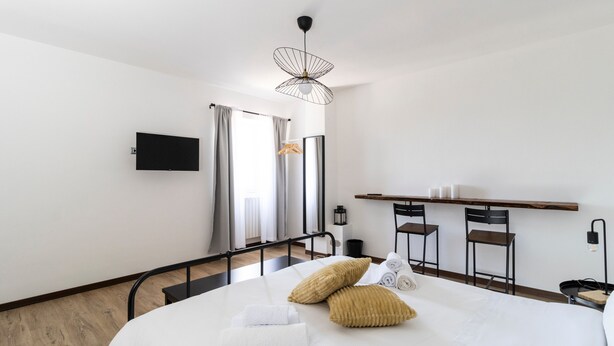 Une chambre d’hôtel équipée d’un lit, d’une télévision, d’un bureau avec des chaises et d’un porte-manteau mural.