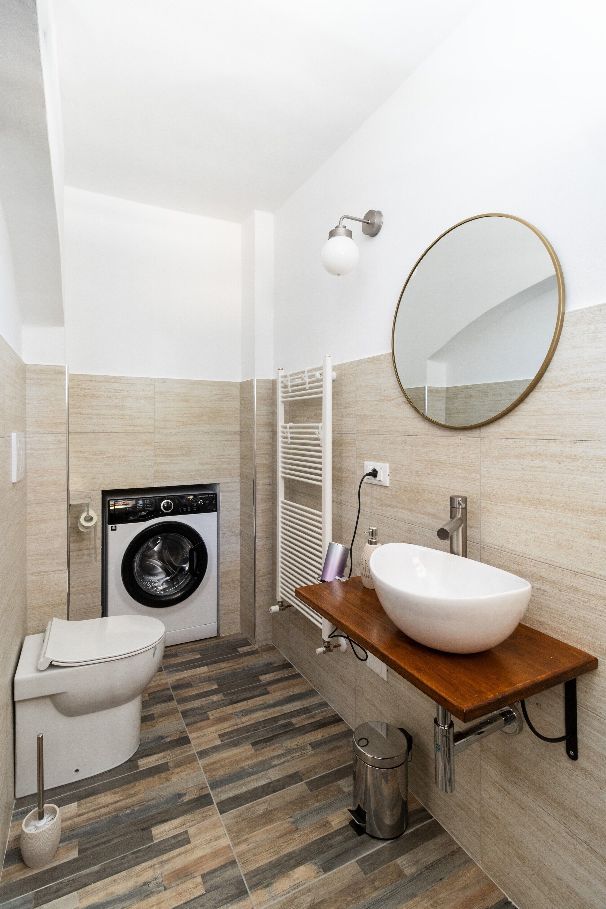 A compact bathroom with a washing machine, toilet, sink, and mirror.