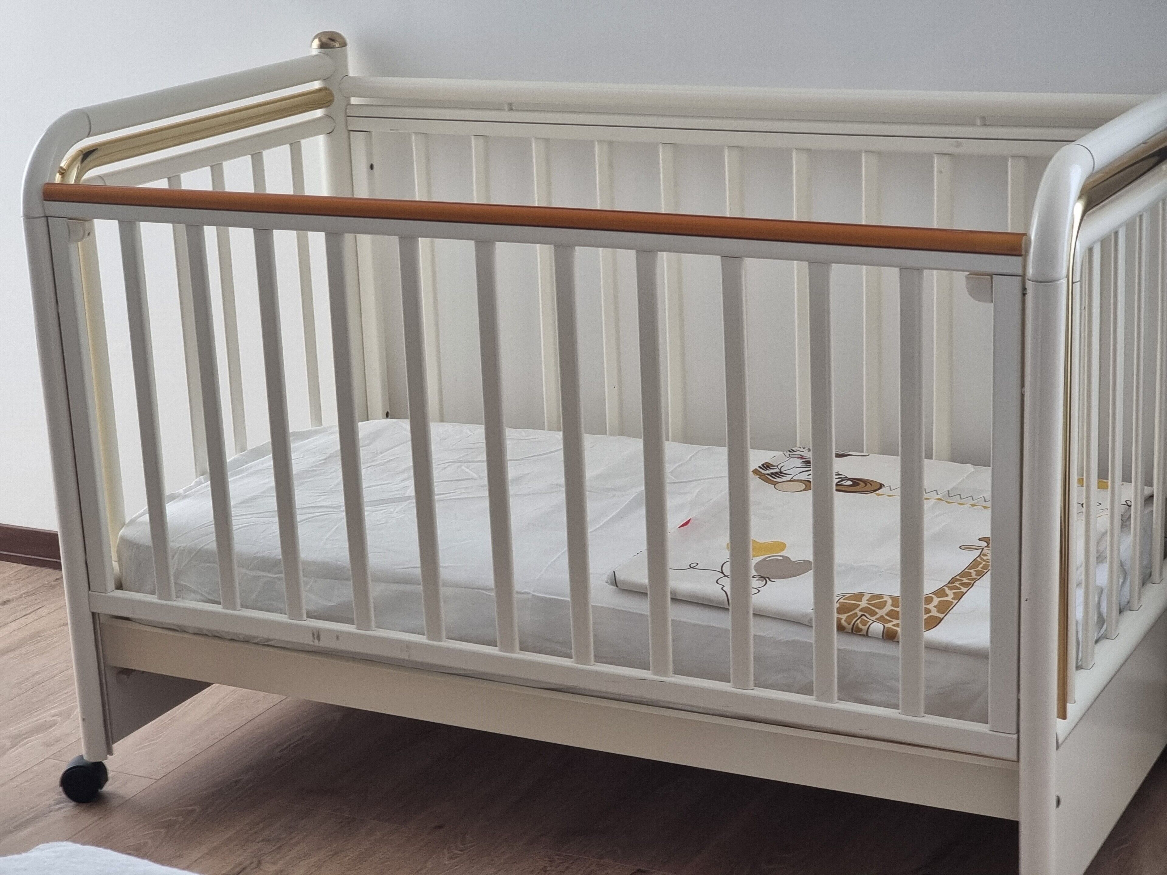 Ein weißes Babybett mit Holz Kopfteil, einer Matratze mit Giraffenmuster und einem weißen Bettlaken.