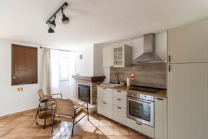 Una cocina con chimenea, horno empotrado y una zona de comedor con sillas de mimbre.