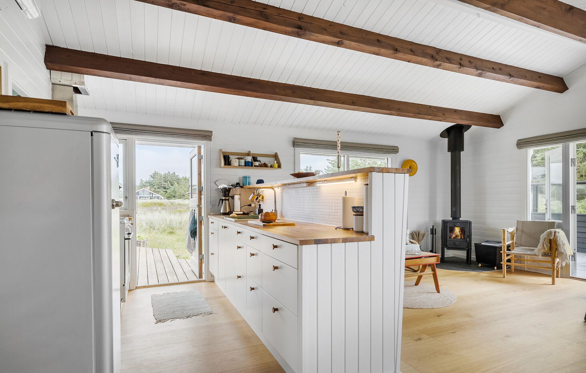 A spacious kitchen with white cabinetry, wooden beams, a central island, and a wood-burning stove.
